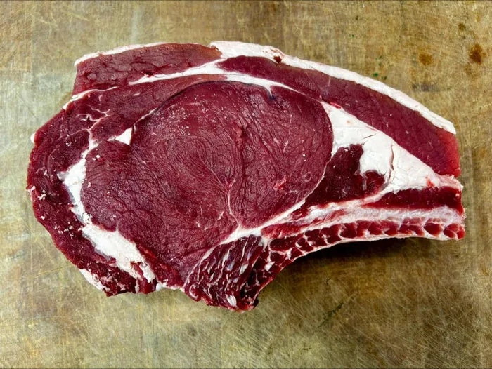 Raw bone-in beef steak from a local Sandbach butcher on a wooden board